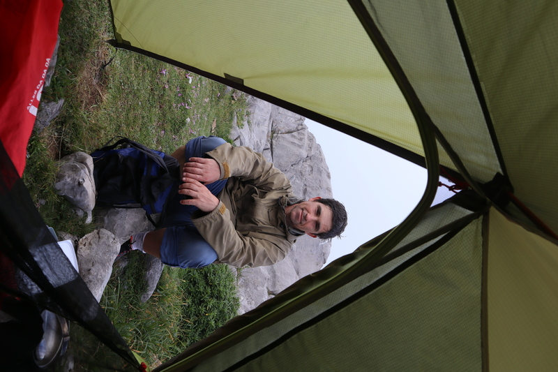 man squatting outside of tent in the fog